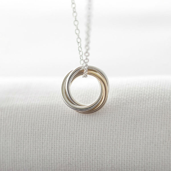 A gold and silver 30th birthday necklace hanging over white material.