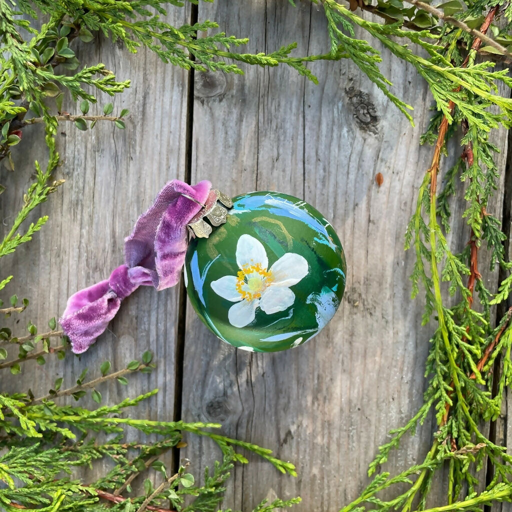 A beautifully hand-painted floral ceramic bauble background painted in dark green adorned in white anemone flowers, finished with a luxurious velvet ribbon.