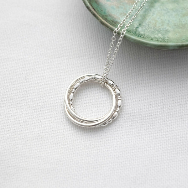 A unique sterling silver 30th birthday necklace displayed on white material with a green jewellery dish in the background.
