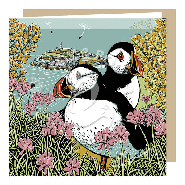 Puffins greeting card by Fox and Boo, two puffins on a clifftop surrounded by gorse and sea thrift, with the backdrop of sea and lighthouse