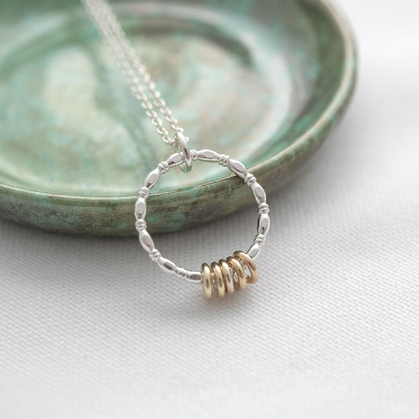A gold and silver 5 ring necklace displayed against a green jewellery dish.