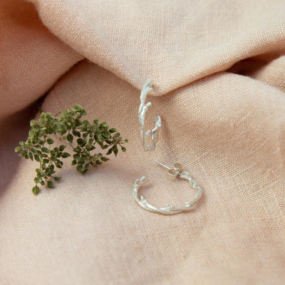 Silver Twisted Twig Hoops on pink cloth near flora