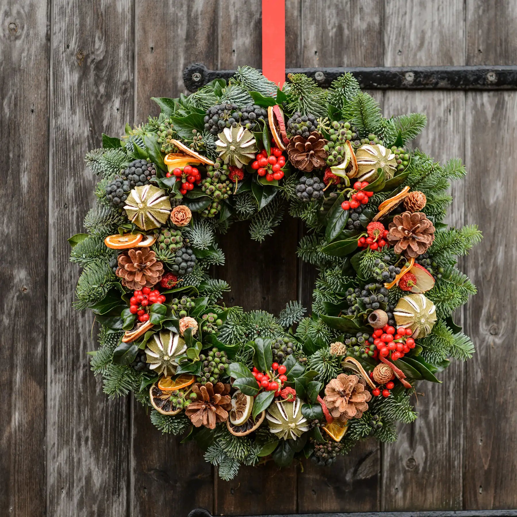 Decorative Christmas wreath with greenery, pinecones, and berries on a wooden door.