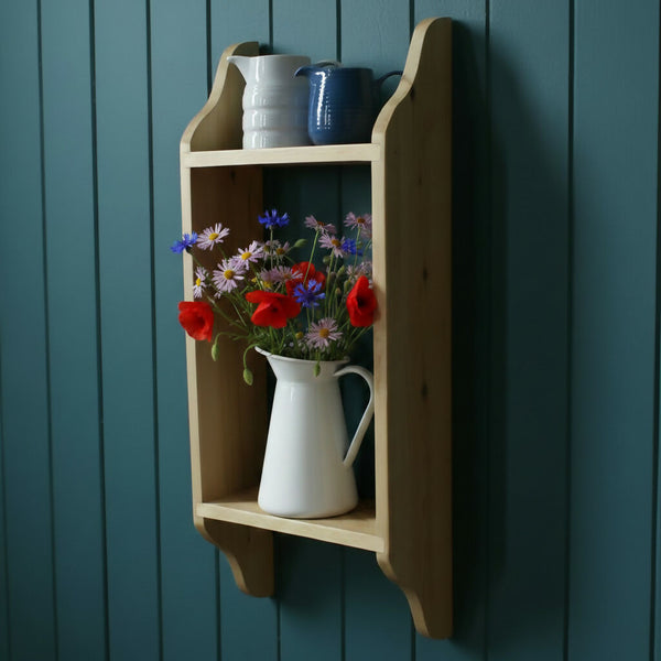 A natural wood two tier shelf aginst a blue wall wih jugs