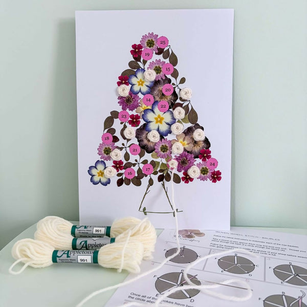 Colour botanical advent calendar embroidery kit with floral Christmas tree design, white yarn, needle and illustrated stitching instructions.
