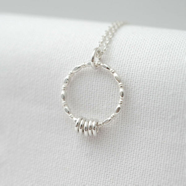 A sterling silver 5 ring necklace displayed over white material.