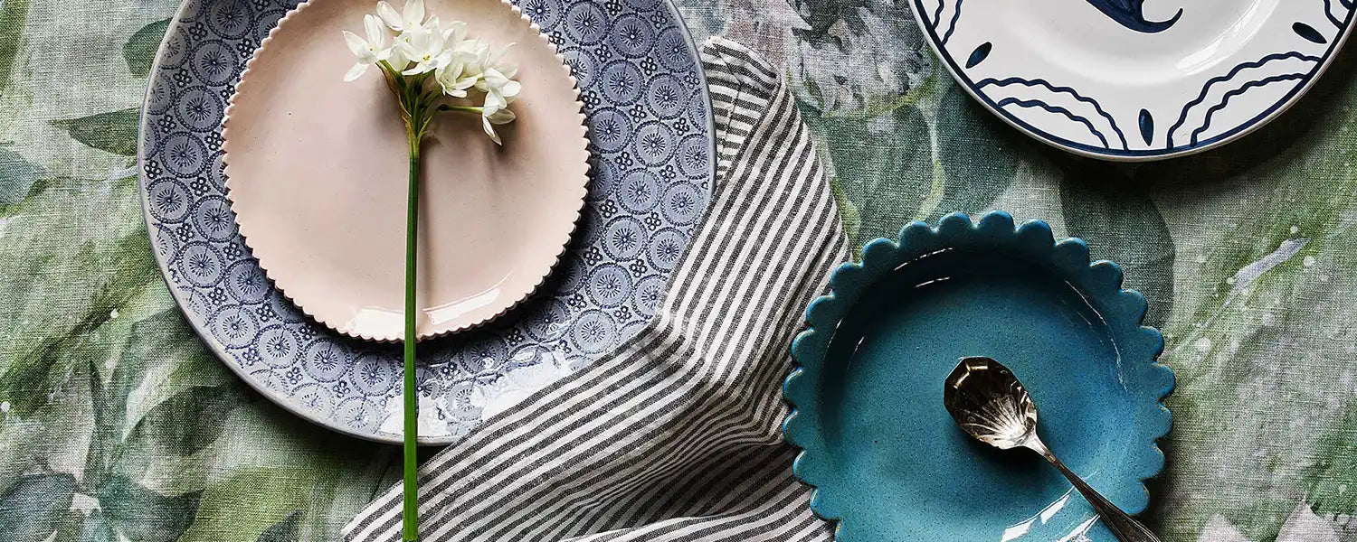 colourful table with country style summer ceramic plates and serveware and a white flower