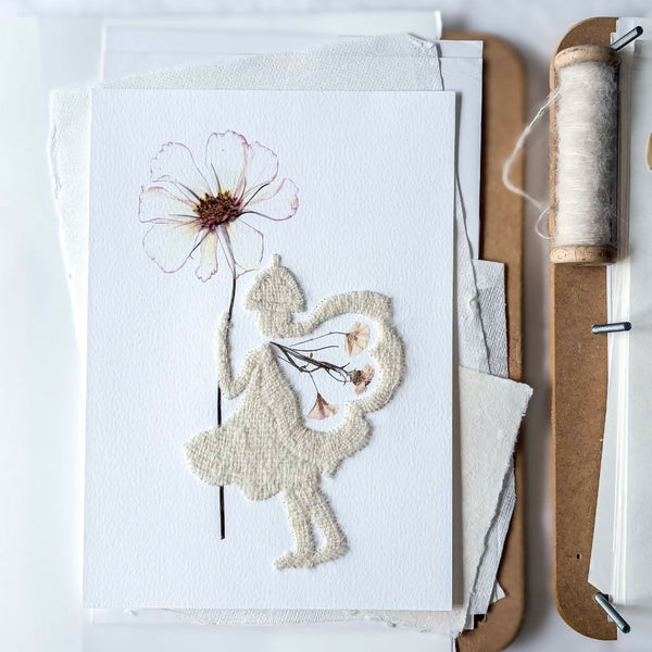 Hand embroidered fairy artwork featuring delicate pressed flowers on textured watercolour paper. A handmade botanical wall art piece with hand embroidered silk and alpaca details, floral fairy wings and a pressed flower wand.
