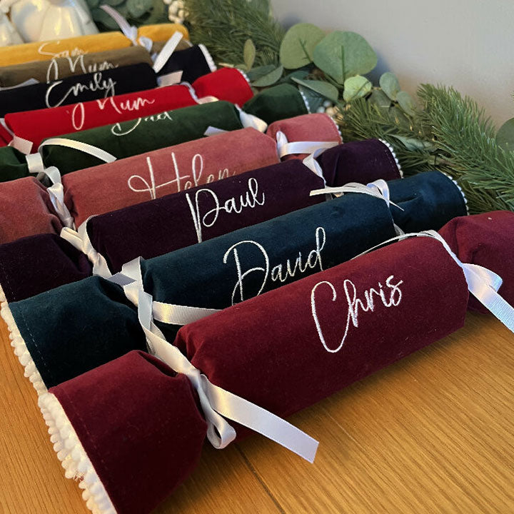 Personalized Christmas cracker names on a wooden surface with greenery in the background