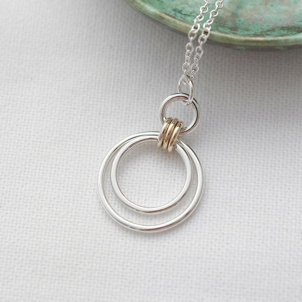 A close up of a three Ring gold and silver Circle Necklace with a green jewellery dish in the background.