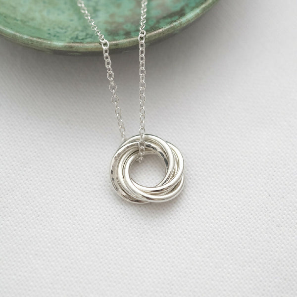 A silver 50th birthday necklace displayed on white material with a green jewellery dish in the background.