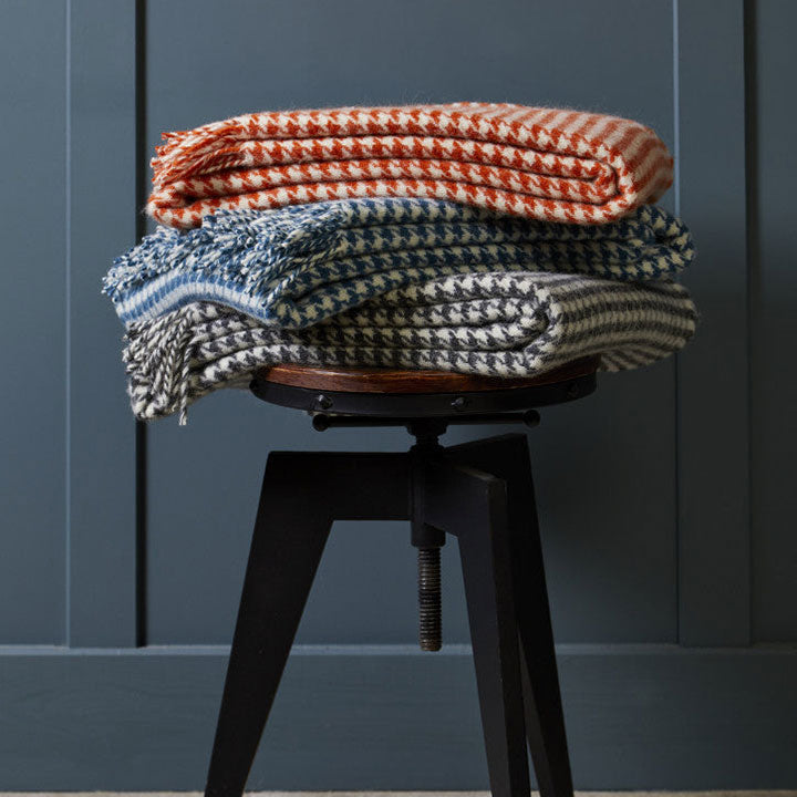 Stack of colorful knitted blankets on a black stool against a dark blue wall.