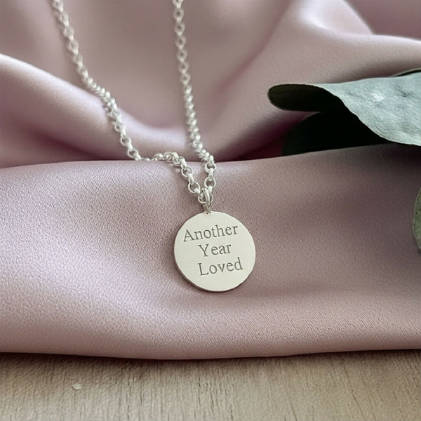 Silver disc charm necklace with “another year loved” engraved in the front