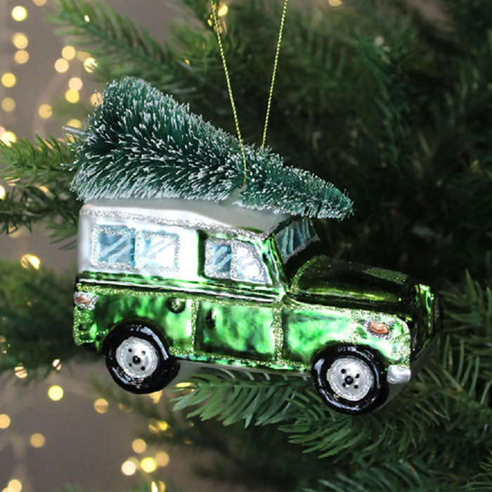 Green car ornament with a tree on top hanging on a Christmas tree.