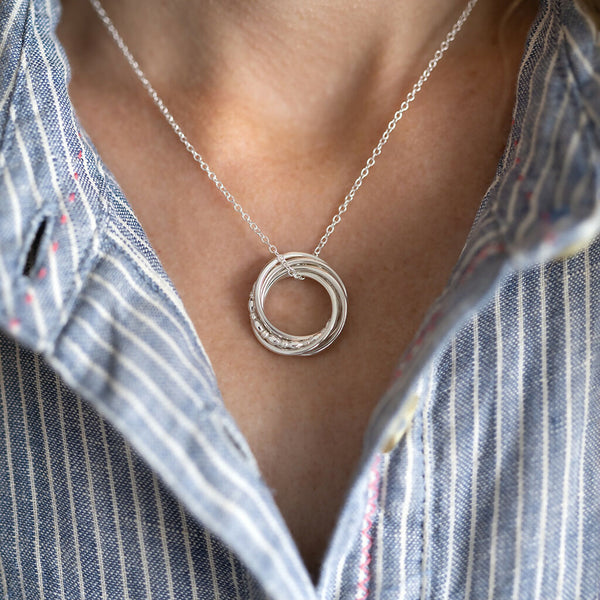 A close up of a person wearing a sterling silver 50th birthday necklace against a blue and white dress.