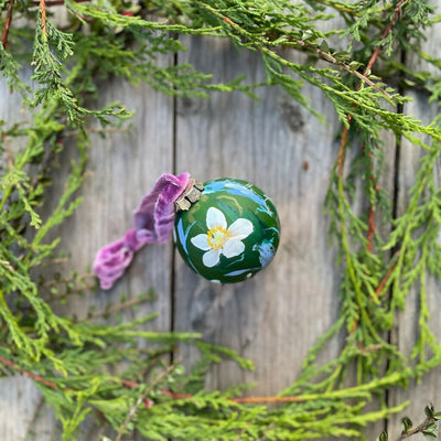 A beautifully hand-painted floral ceramic bauble background painted in dark green adorned in white anemone flowers, finished with a luxurious velvet ribbon.