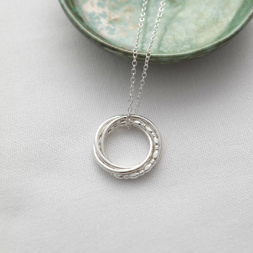 A silver 4 ring necklace displayed on white material with a green jewellery dish in the background.