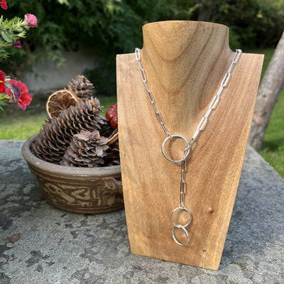 Handmade sterling silver lariat necklace on a chunky silver paperclip chain, displayed on a wooden bust with a natural background