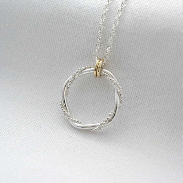 A silver entwined ring necklace with two gold rings displayed against white material.