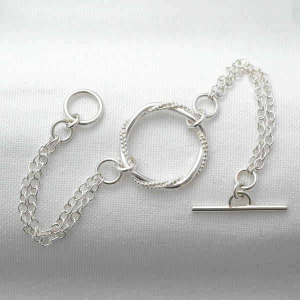 A unique sterling silver entwined ring bracelet with toggle clasp fastening displayed on white material.