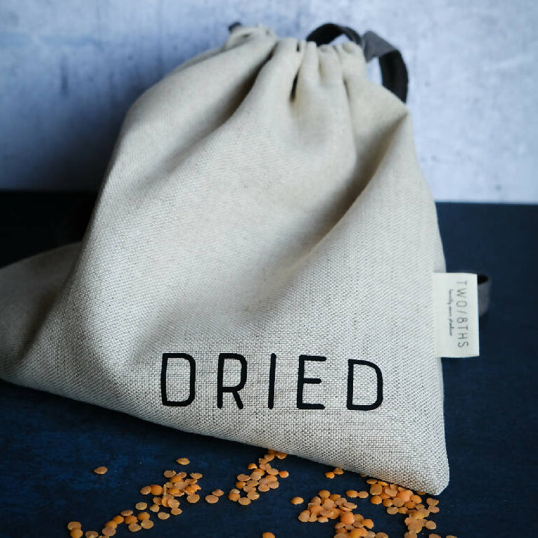 A linen produce bag printed with the word Dried, and shown with red lentils.