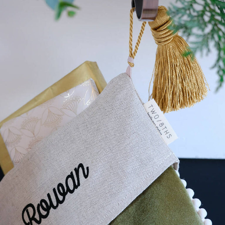 A personalised christmas stocking being hung by a large gold tassel.