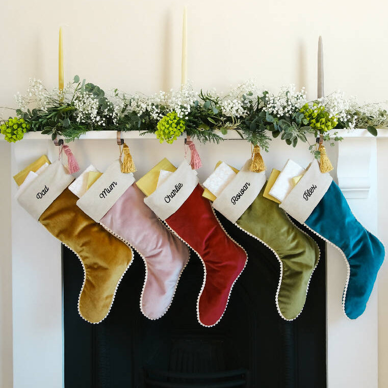 A family'e christmas stockings in velvet hung  from the fireplace.