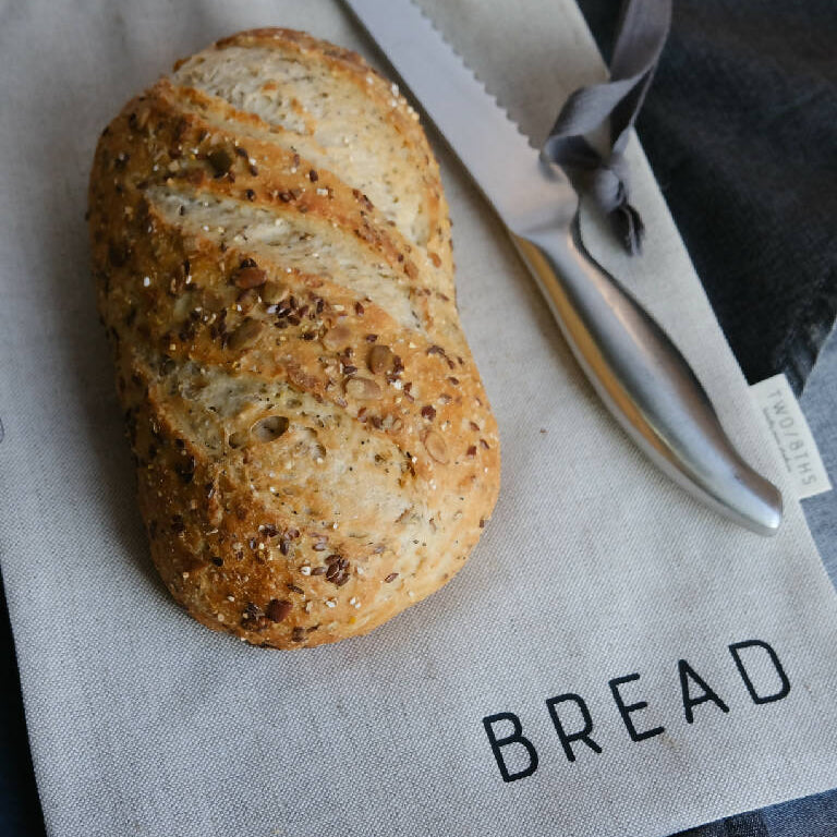 A loaf of bread sat on top of a linen bread bag, and next to a bread knife.