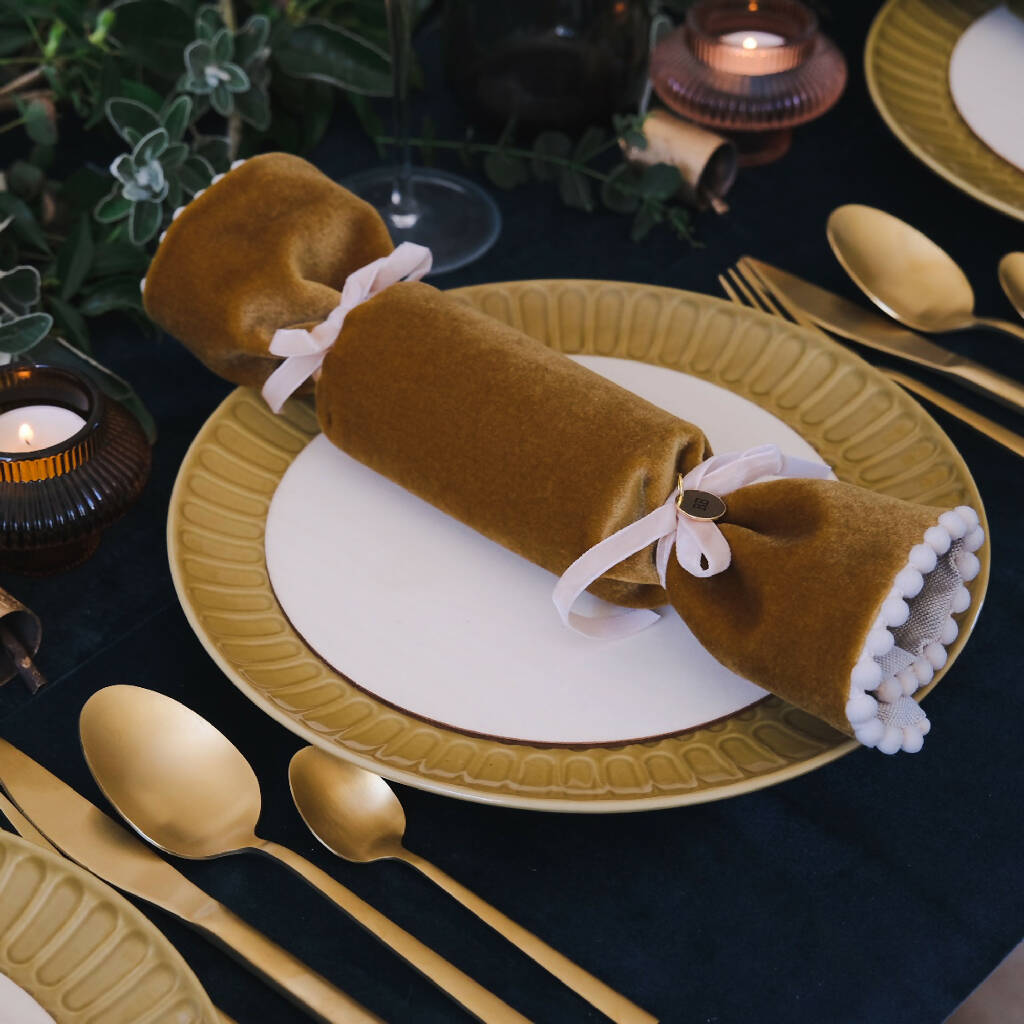 A gold velvet fabric reusable cracker placed on a dinner plate.