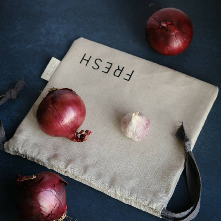 Linen produce bag printed with the word Fresh, and shown with red onions.