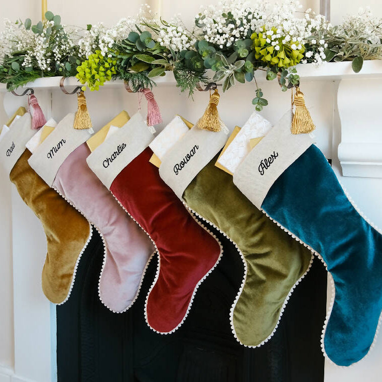 Five velvet christmas stockings with pompom trim hung from the fireplace.