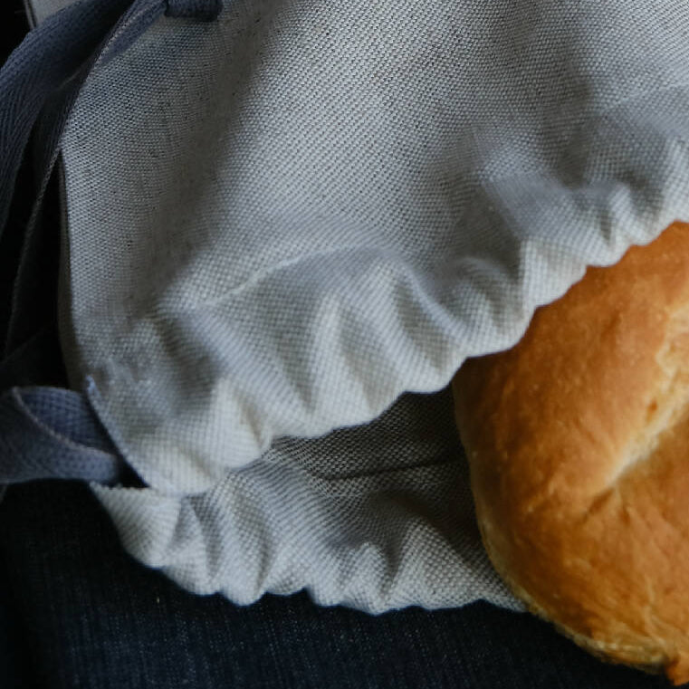 A linen bread bag, shown with a loaf poking out the top, and a drawstring closure.