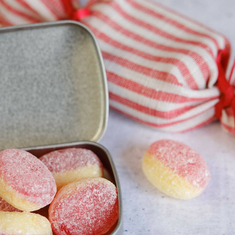 An open tin with sweets inside, next to a fabric wrapped humbug
